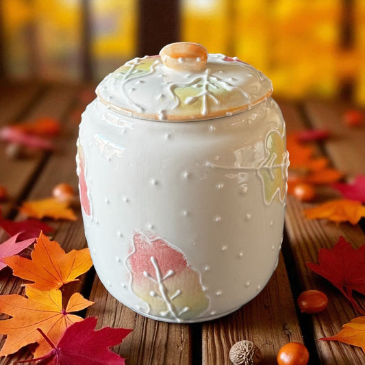 Ceramic jar with autumn leaf design on a wooden surface with autumn leaves