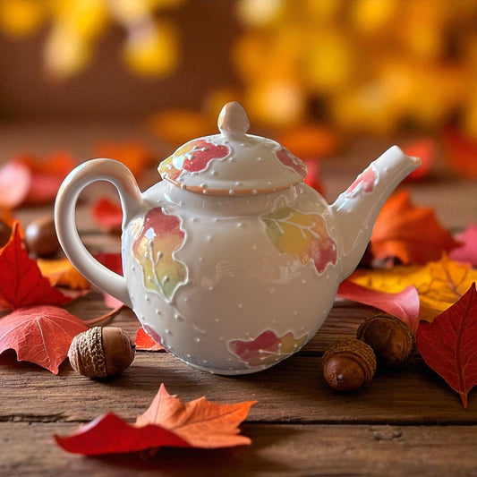 Decorative teapot with autumn leaf design on a wooden surface with fall leaves and acorns.