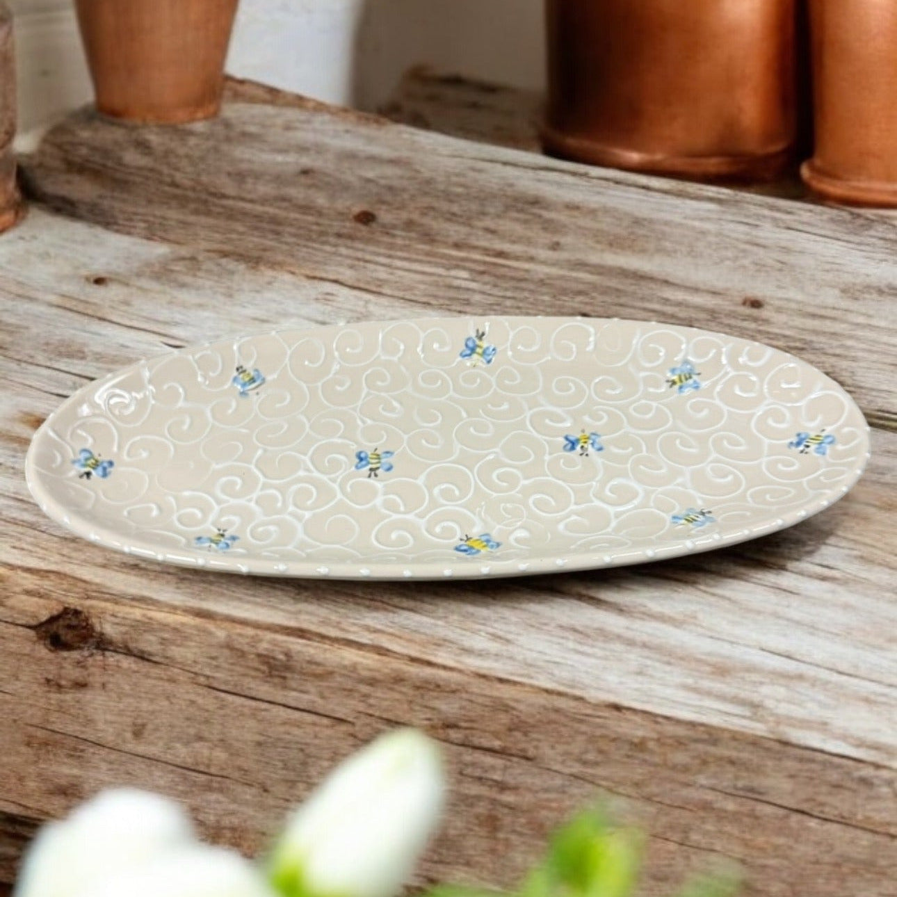 An oval ceramic serving dish with hand-painted floral patterns on it, displayed on a wooden table.