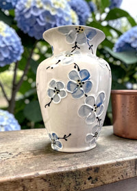 Ceramic vase with floral blue Cherry Blossom design on a wooden surface with blue flowers in the background