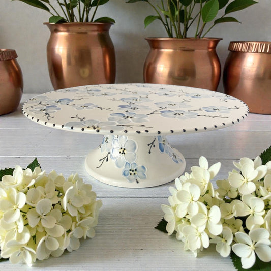 Decorative cake stand with blue cherry blossom floral design on a white surface with copper planters and white flowers.