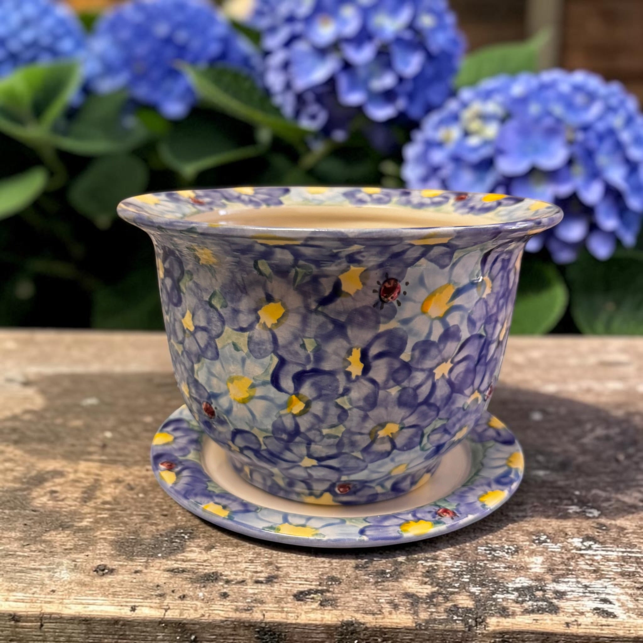 Decorative  blue daisy ceramic pot with floral pattern on a wooden surface with blue flowers in the background | Ladybird Ceramics Canada