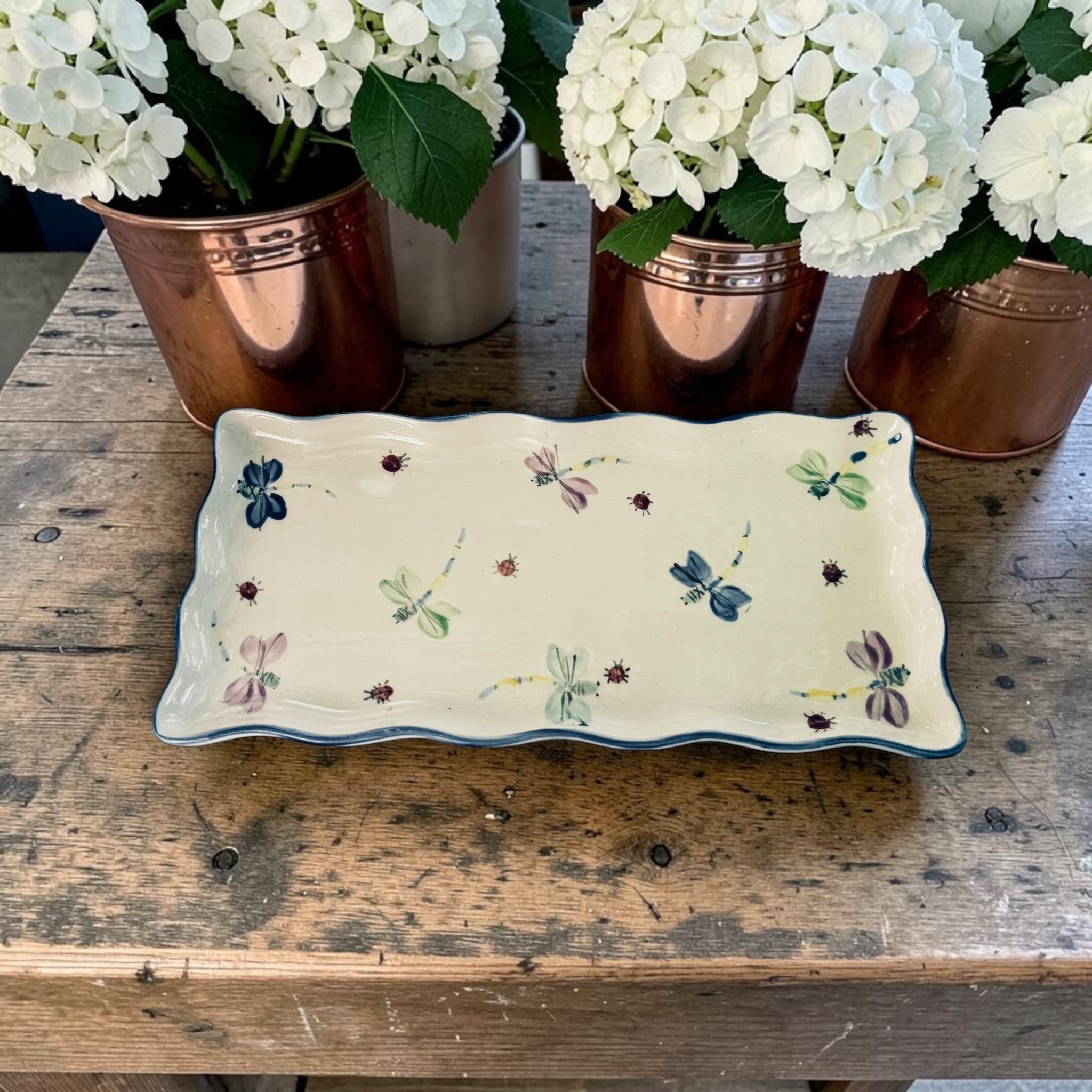 Decorative tray with blue accent and dragonfly patterns on a wooden surface with potted white flowers. Ladybird Ceramics Canada