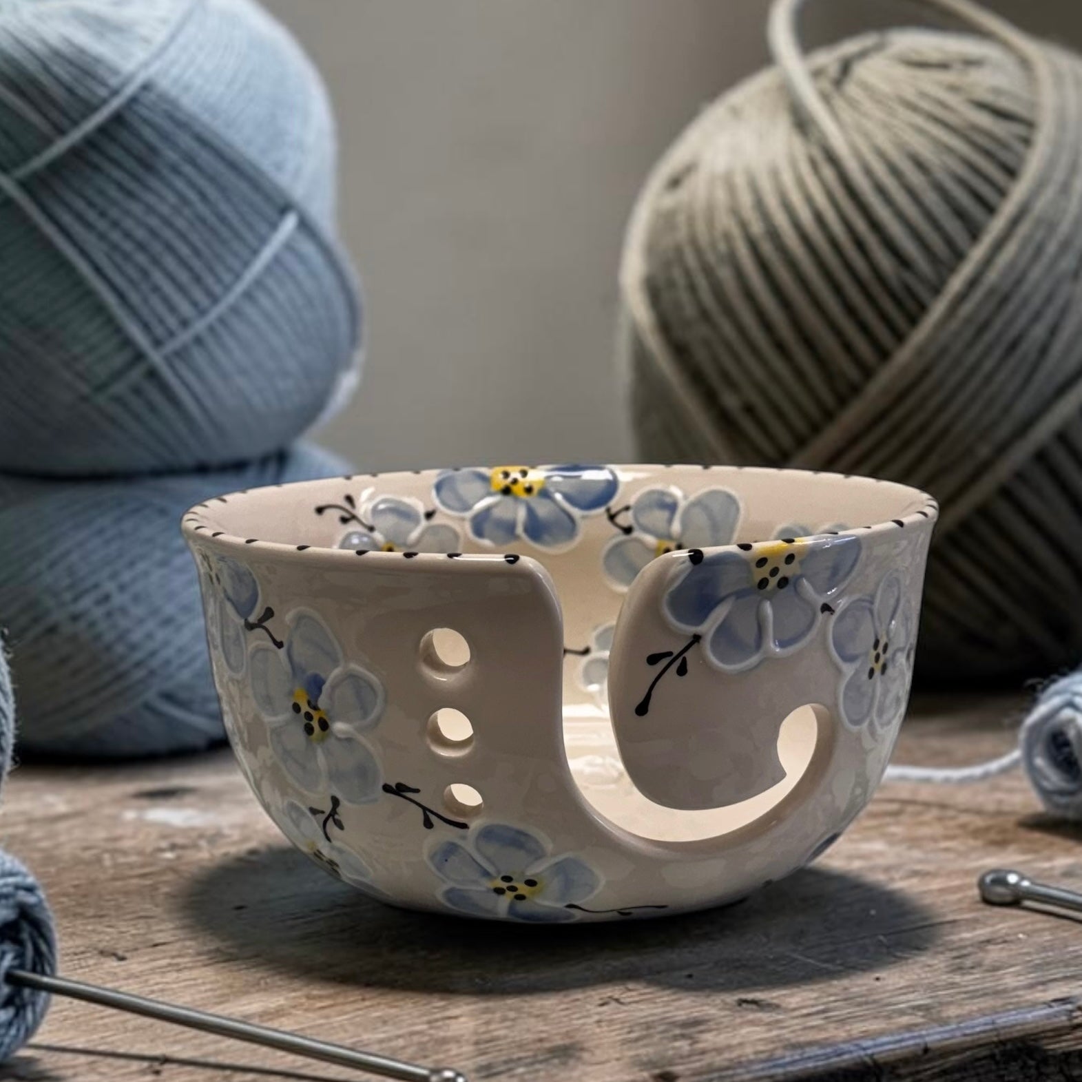 Decorative blue cherry blossom  ceramic yarn bowl with floral patterns on a wooden surface with yarn and knitting needles | Ladybird Ceramics Canada