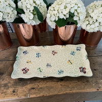 Decorative tray with painted butterfly pattern on a wooden surface with white flowers in copper pots.