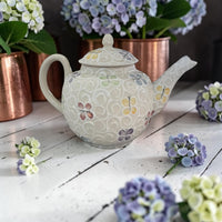 Decorative teapot with butterfly pattern on a wooden surface with flowers around