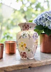 Floral-patterned cherry blossom handpainted vase with copper planters and hydrangeas on a wooden surface