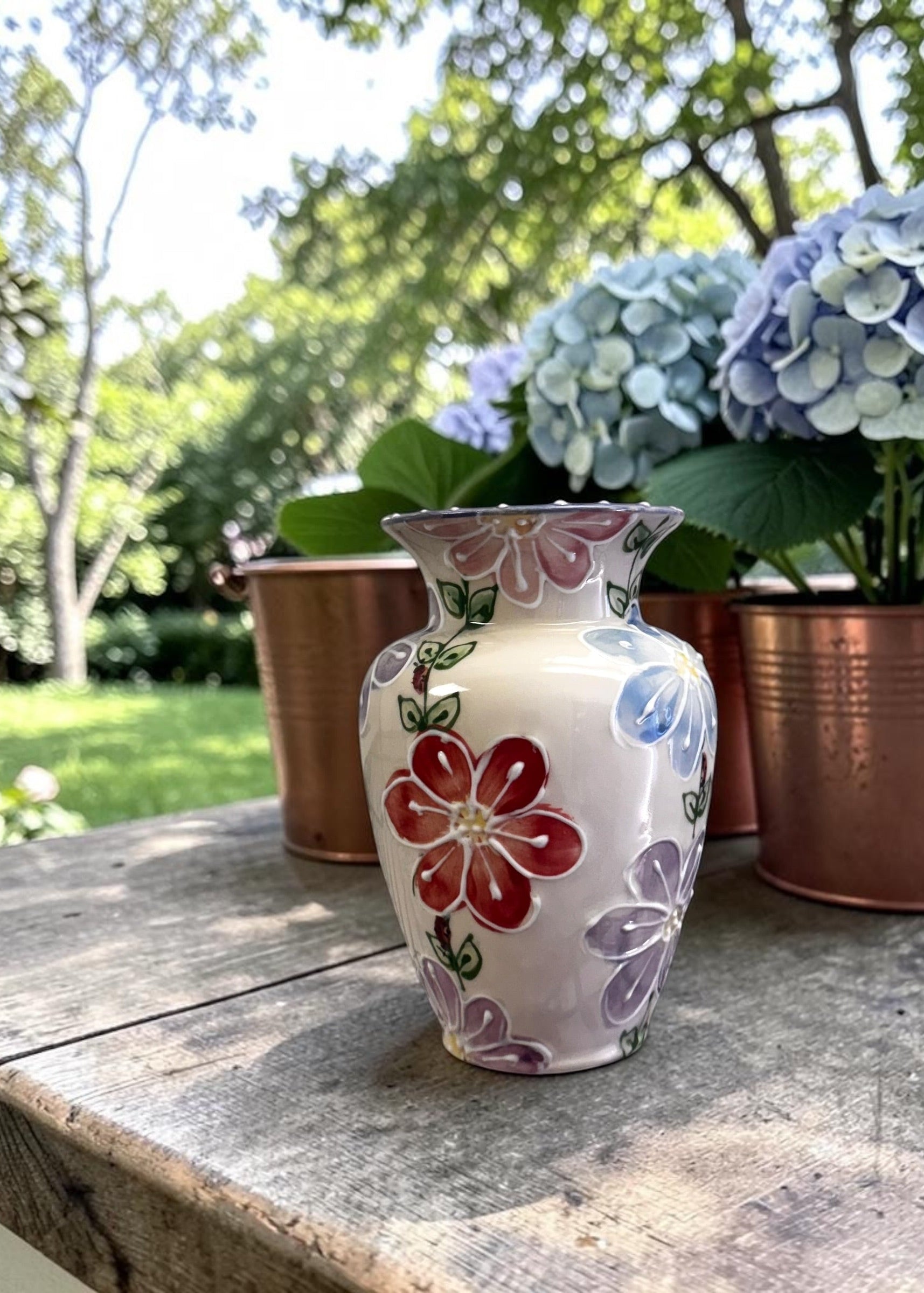 Hand-painted daisy floral vase on a wooden surface with hydrangeas in the background made in Canada