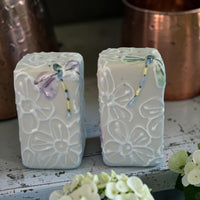 Two decorative salt and pepper shakers with dragonfly motif with floral patterns on a wooden surface.