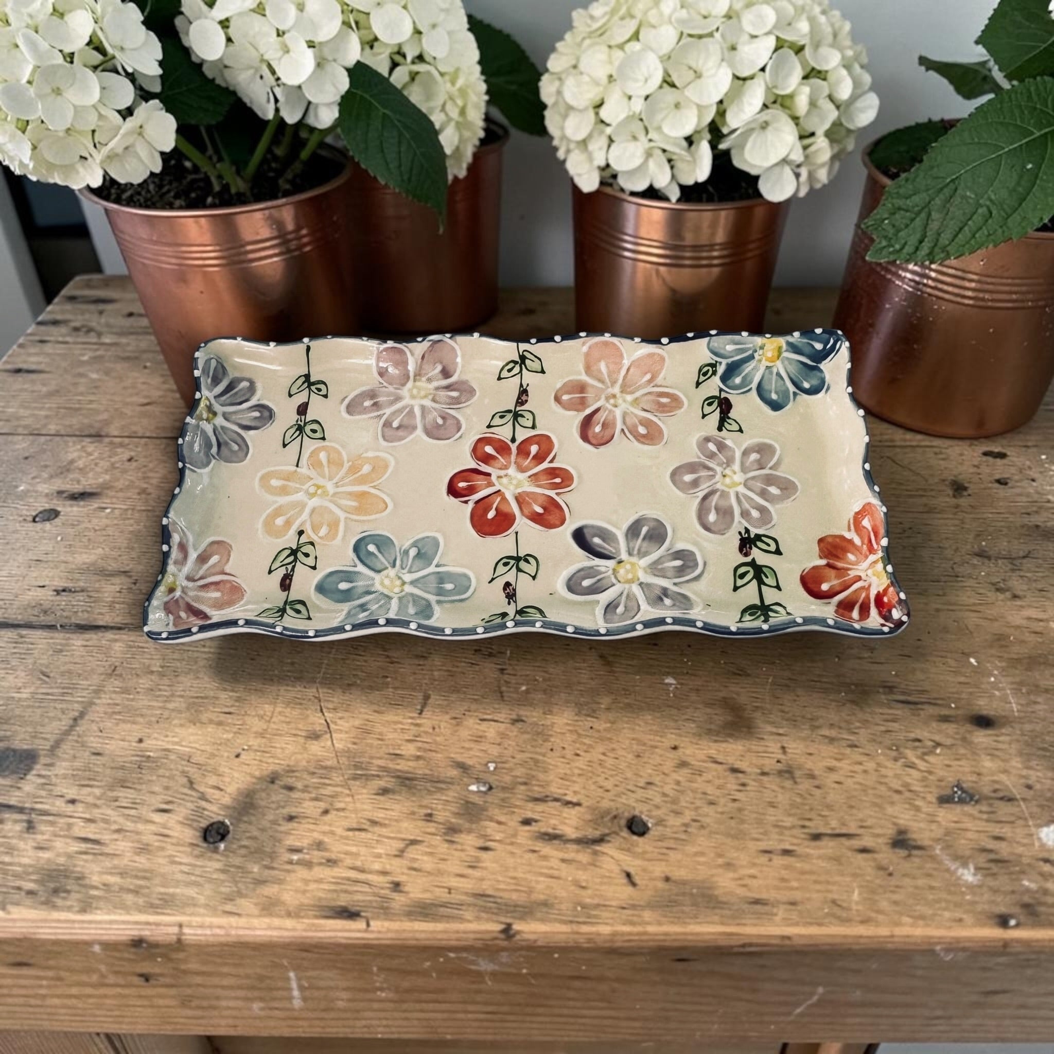 Decorative tray with floral design on a wooden surface with potted plants in the background