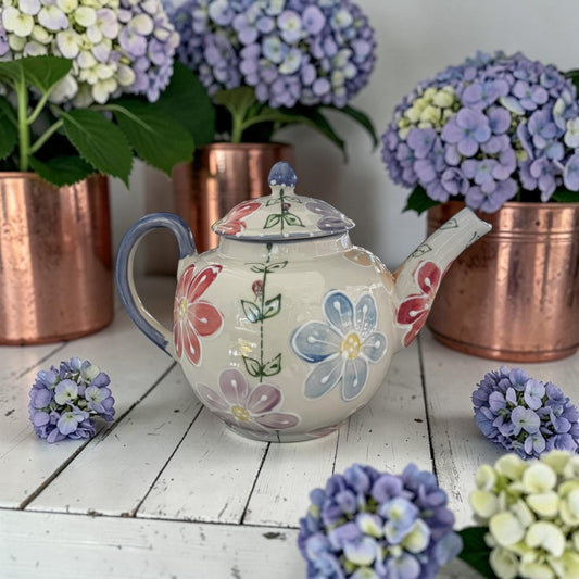 Floral teapot daisy pattern on a wooden surface with potted hydrangeas in the background
