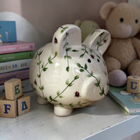 Green Leaves decorative piggy bank with floral patterns on a surface with books and a teddy bear in the background - Ladybird Ceramics