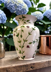 Decorative vase with floral patterns on a wooden surface with hydrangeas in the background