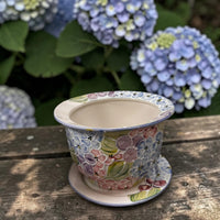 Decorative ceramic pot with floral pattern on a wooden surface with hydrangeas in the background | Ladybird Ceramics Canada