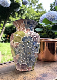Decorative mosaic vase on a wooden surface with a garden background