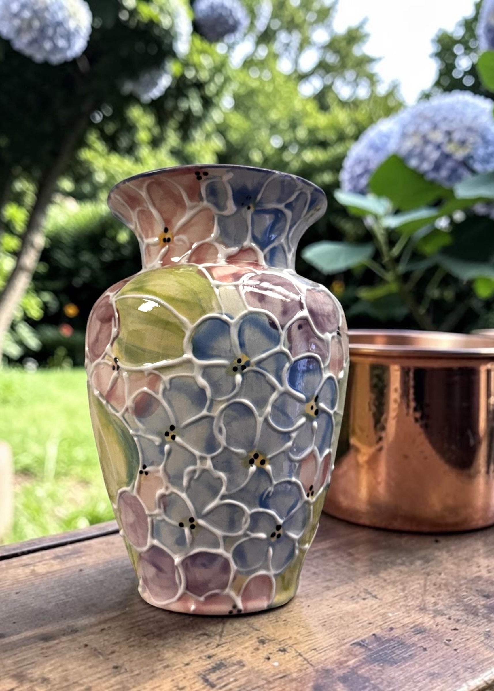 Decorative mosaic vase on a wooden surface with a garden background