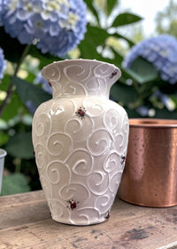 White decorative vase with ladybug patterns on a wooden surface with blue flowers in the background