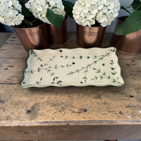 Decorative ceramic tray with floral design on a wooden surface with potted plants.