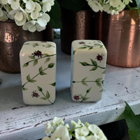 Two decorative ceramic salt and pepper with floral patterns on a wooden surface with white flowers in the background.