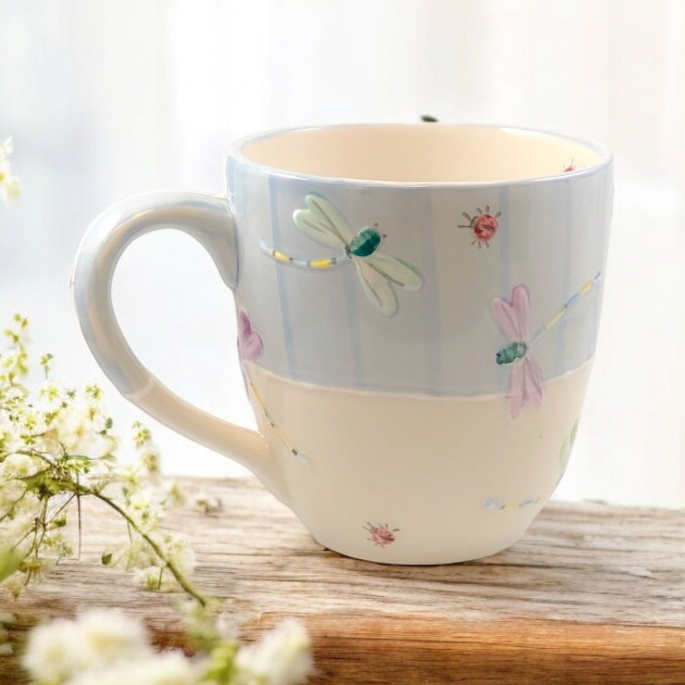 Hand painted ceramic extra large mug with floral patterns and a handle, displayed on a wooden surface with flowers in the background.
