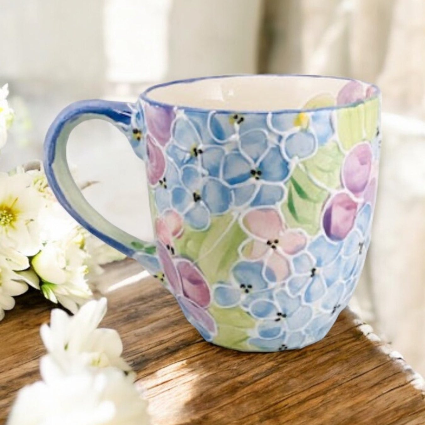 Hand painted ceramic extra large mug with floral patterns and a handle, displayed on a wooden surface with flowers in the background.