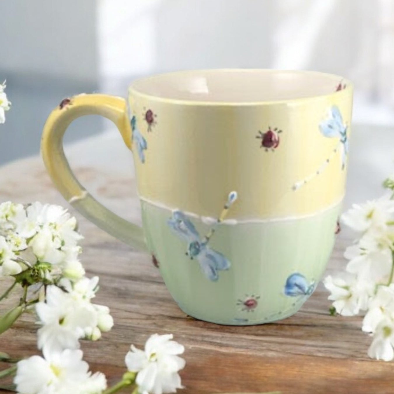 Hand painted ceramic extra large mug with floral patterns and a handle, displayed on a wooden surface with flowers in the background.