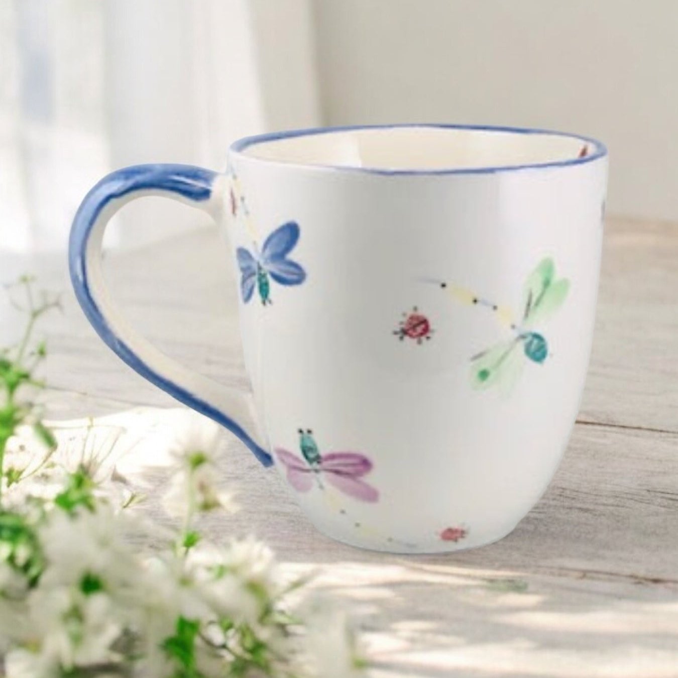 Hand painted ceramic extra large mug with floral patterns and a handle, displayed on a wooden surface with flowers in the background.