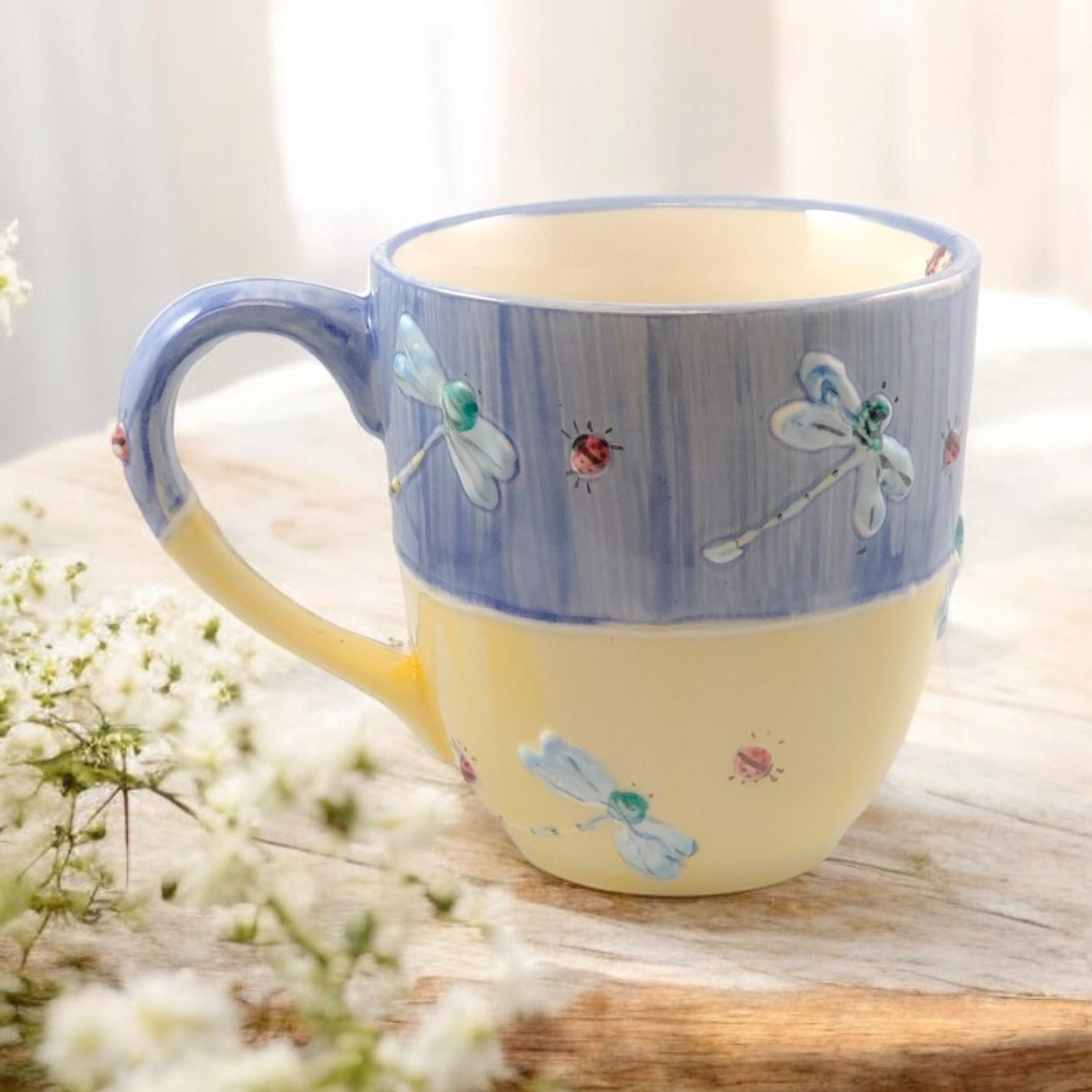 Hand painted ceramic extra large mug with floral patterns and a handle, displayed on a wooden surface with flowers in the background.