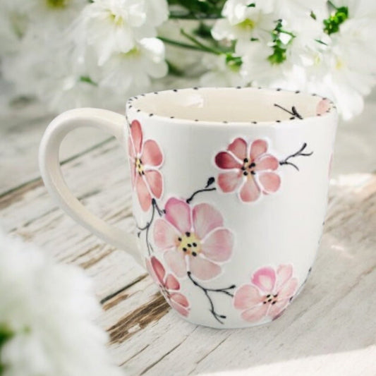 Hand painted ceramic extra large mug with floral  pink patterns and a handle, displayed on a wooden surface with flowers in the background.