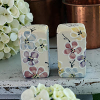 Two ceramic salt and pepper shakers with floral designs on a wooden surface.