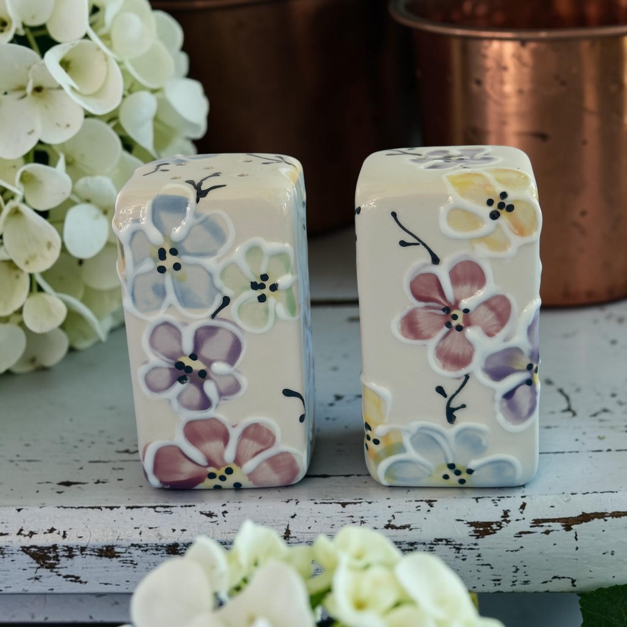 Two ceramic salt and pepper shakers with floral designs on a wooden surface.
