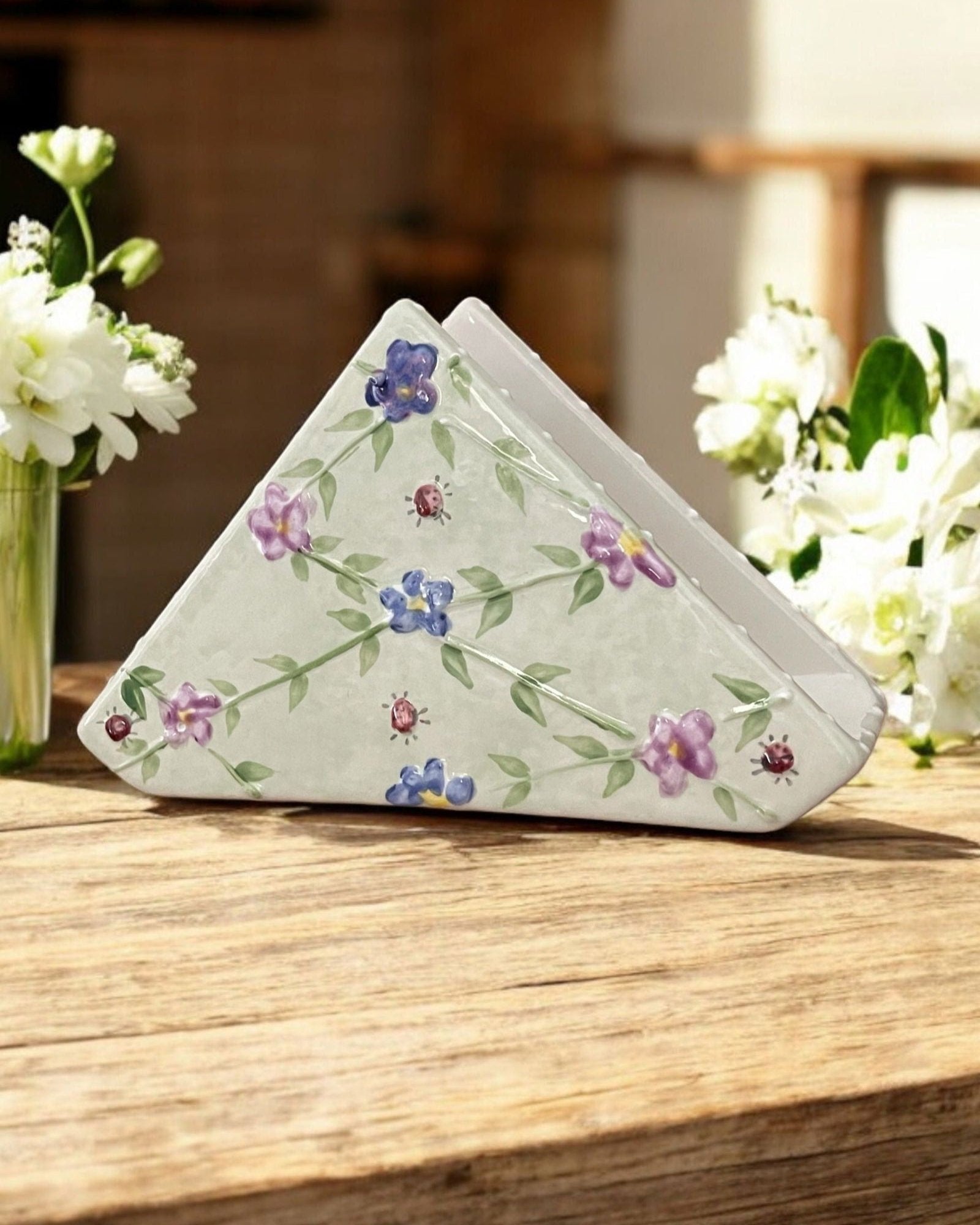 A triangular white ceramic napkin holder with embossed  floral patterns displayed on a wooden table.