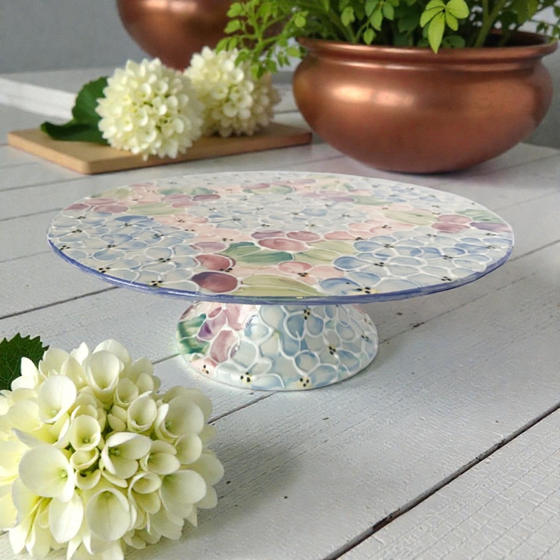 Decorative cake stand withNew hydrangea floral pattern on a wooden surface with flowers and plant pots.