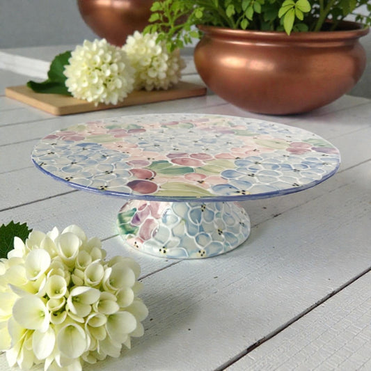 Decorative cake stand withNew hydrangea floral pattern on a wooden surface with flowers and plant pots.