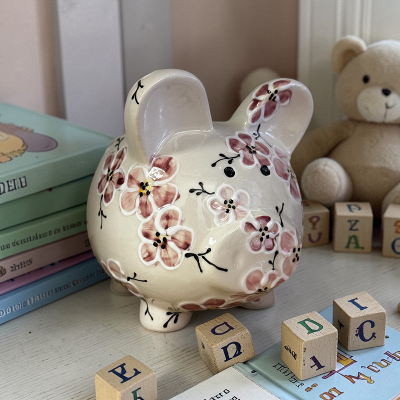 Pink Cherry Blossom Floral-patterned piggy bank on a surface with books and blocks in the background - Ladybird Ceramics