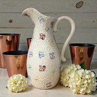 Decorative ceramic pitcher with butterfly patterns on a wooden surface with copper cups and flowers. Ladybird Ceramics