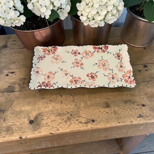 Floral-patterned tray on a wooden surface with potted plants in the background