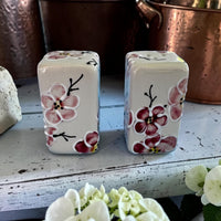 Two ceramic  cherry blossom salt and pepper shakers with floral designs on a wooden surface.