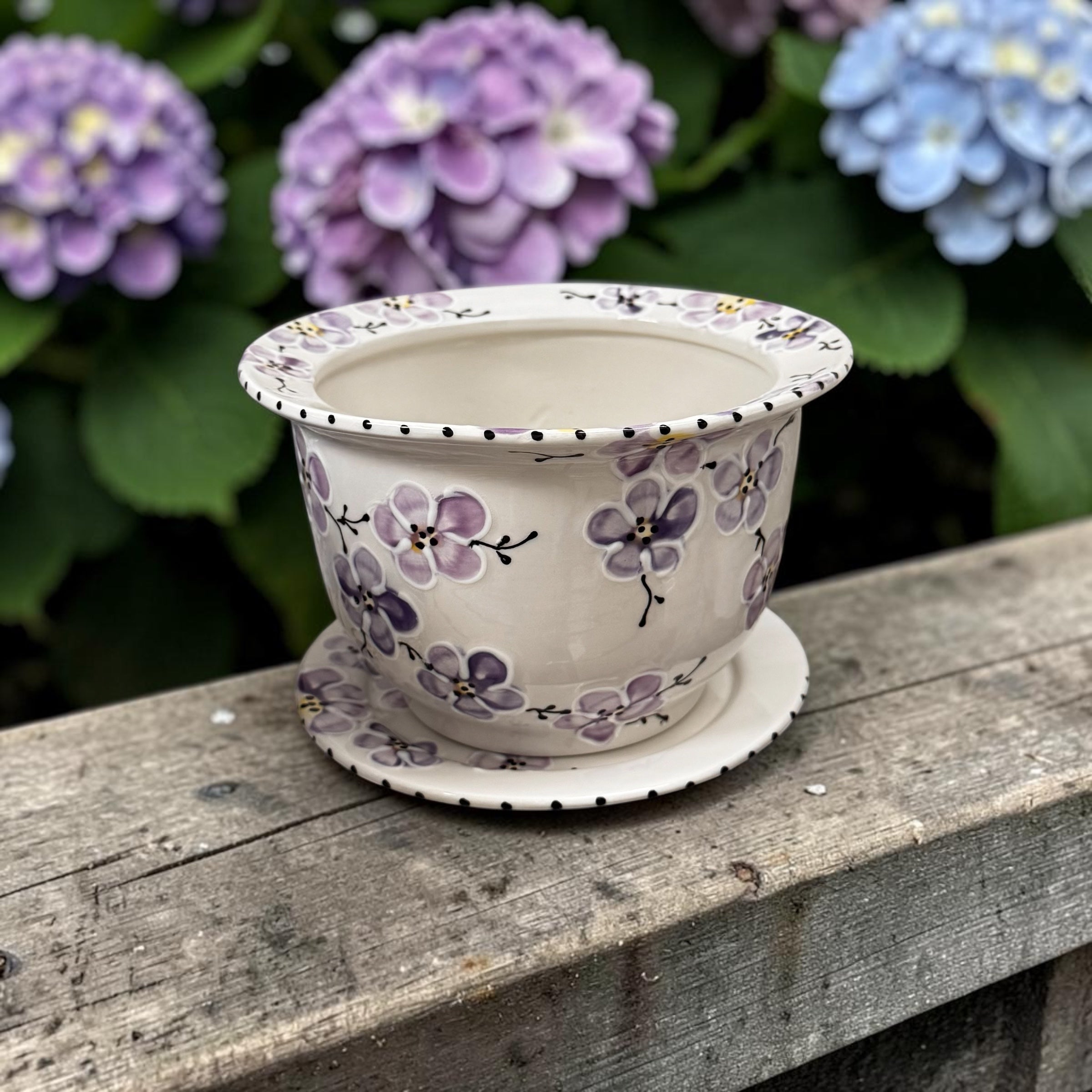Ceramic flowerpot with purple cherry blossom floral design on a wooden surface with hydrangeas in the background | Ladybird Ceramics Canada