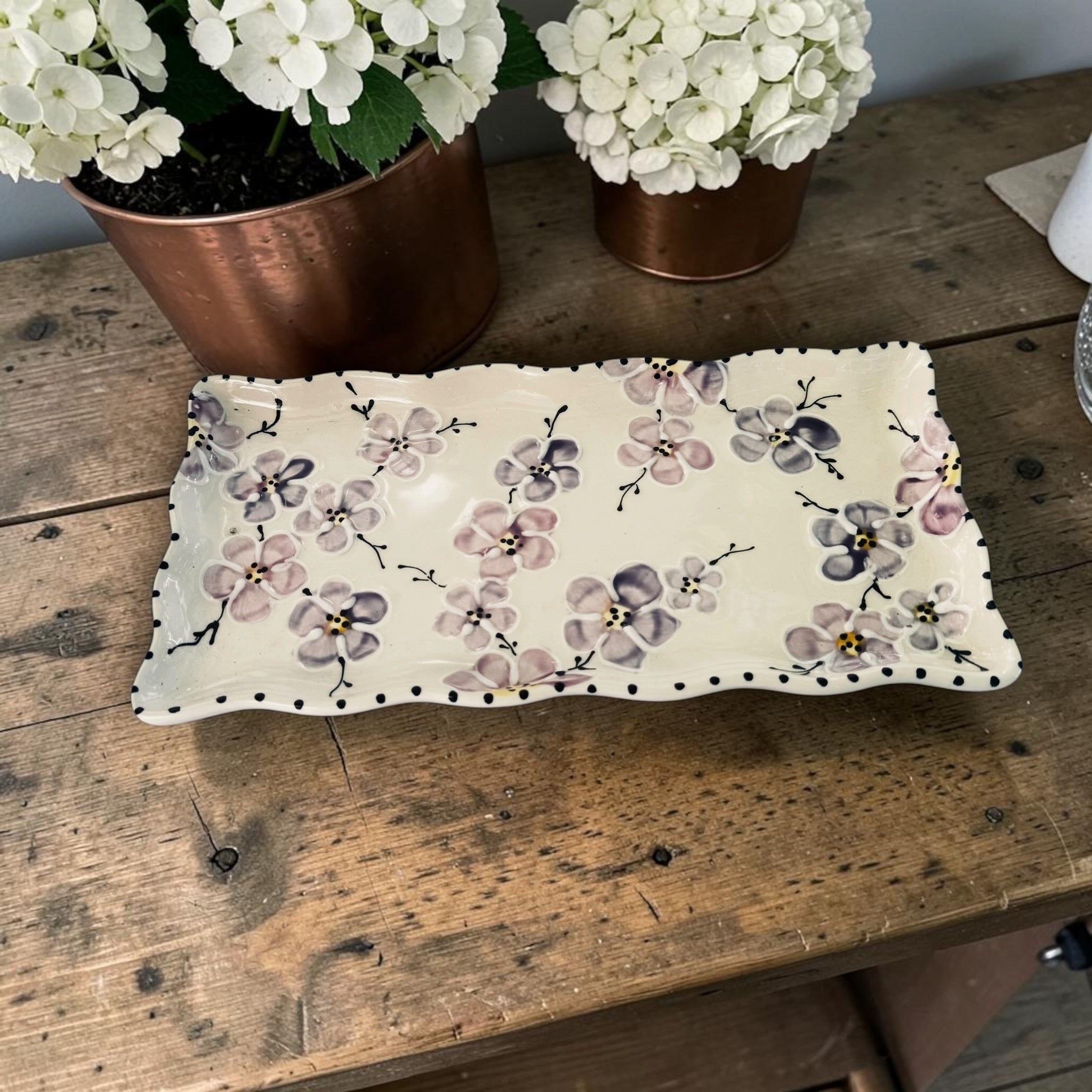 Floral-patterned ceramic tray with ruffle edge on a wooden surface with potted plants in the background Ladybird Ceramics Canada 