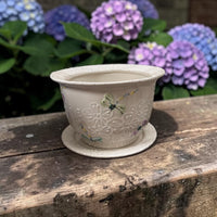 Ceramic planter with floral design and dragonfly on a wooden surface with hydrangeas in the background  Ladybird Ceramics Canada