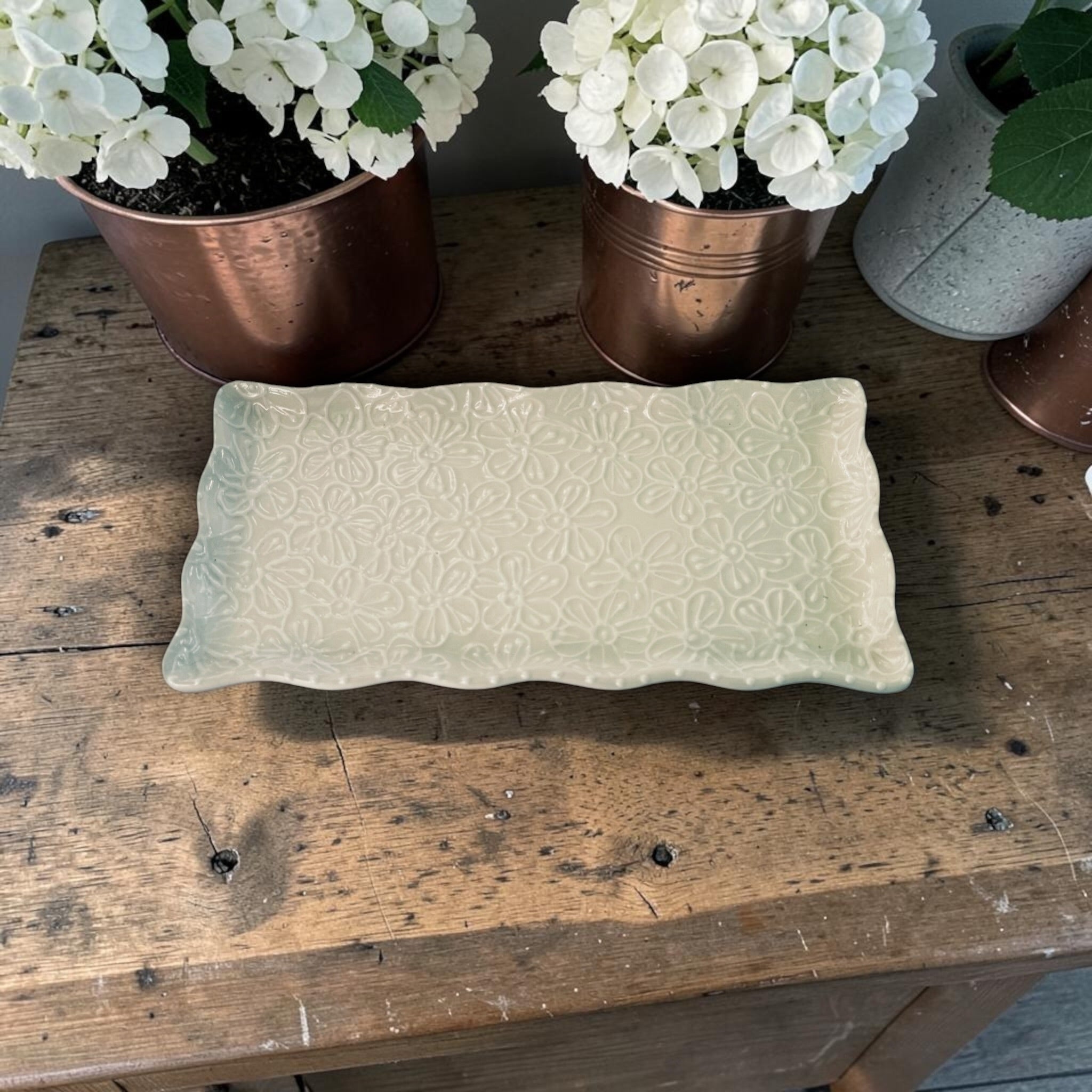 Decorative rectangular ceramic platter with ruffle edge  on a wooden surface with potted plants in the background. Ladybird Ceramics Canada 