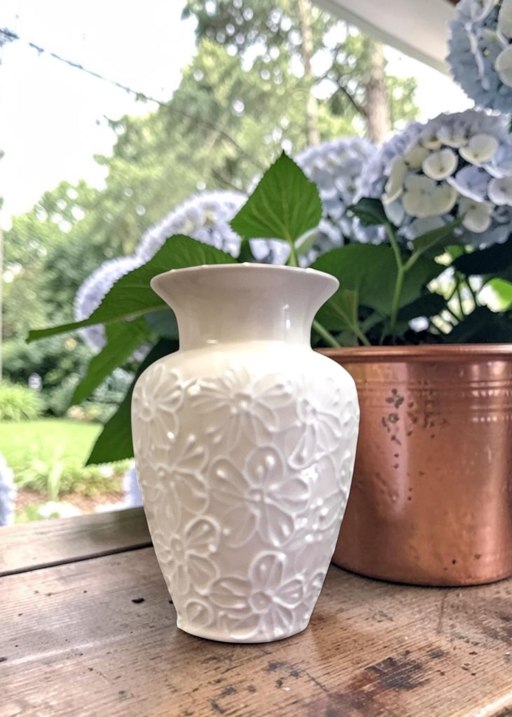 White textured vase on a wooden surface with hydrangeas in the background