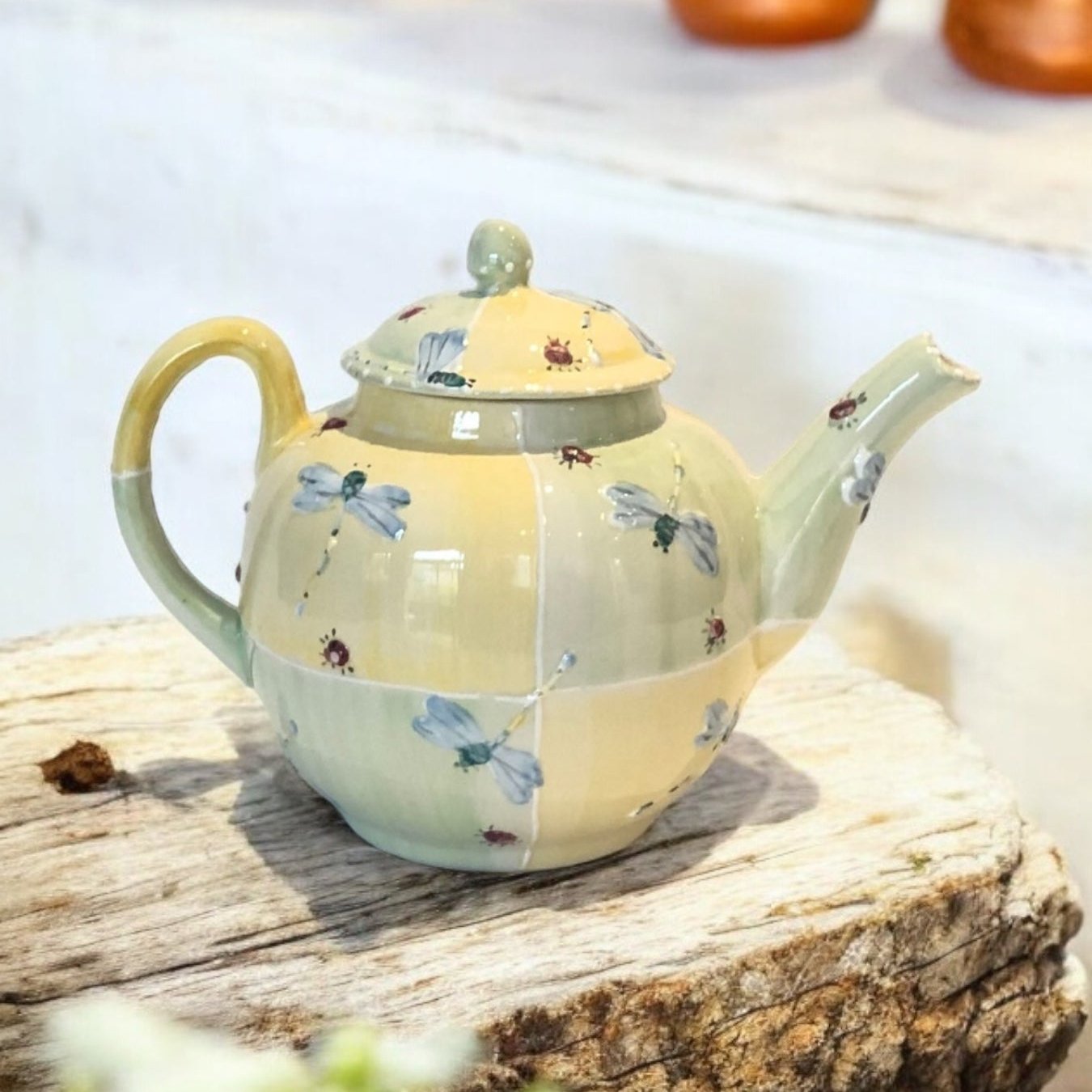A white ceramic teapot with hand-painted floral designs, displayed on a wooden surface with a bouquet of white flowers beside it.