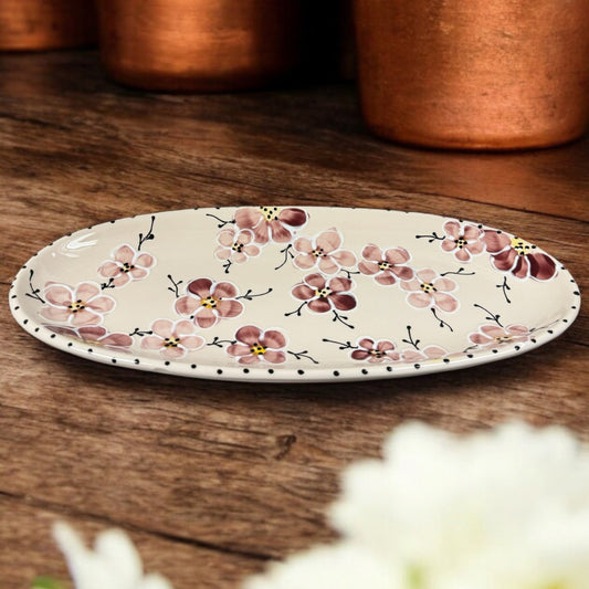 An oval ceramic serving dish with hand-painted floral patterns on it, displayed on a wooden table.