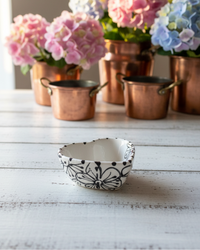 Decorative bowl with butterfly design on a wooden surface with potted flowers in the background.