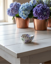Copper pots with blue and purple flowers on a white wooden table.
