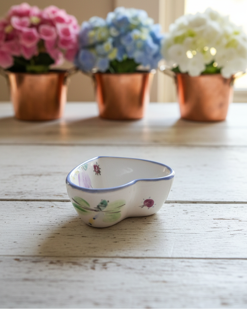 Decorative ceramic bowl with floral design on a wooden surface, with potted flowers in the background.