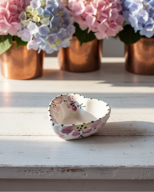 Small ceramic bowl with floral design on a wooden surface, with flowers in copper pots in the background.