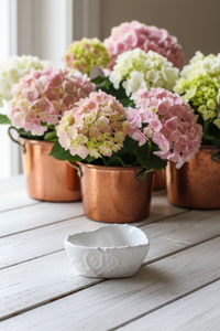 Decorative arrangement of pink, green, and white flowers in copper pots on a wooden surface.